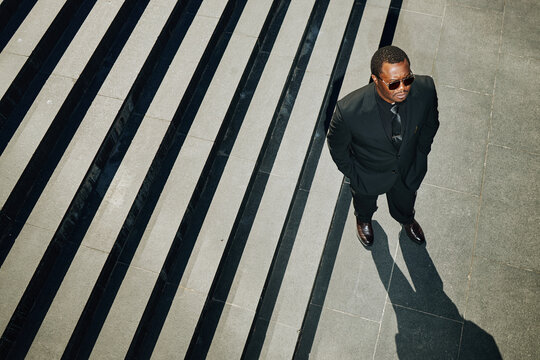 High angle shot of African American businessman standing near stairs, looking upward and projecting leadership and ambition. Ideal for corporate branding, career growth campaigns