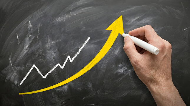Hand drawing upward yellow arrow and white line graph on black chalkboard with white chalk