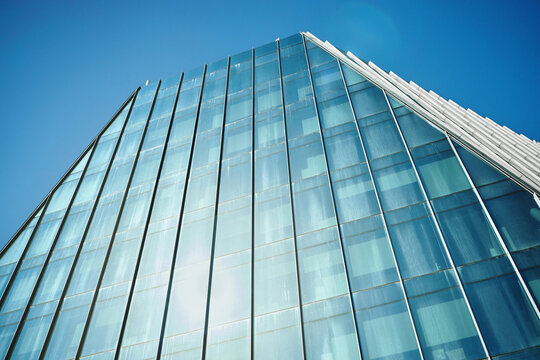 Low angle view of modern glass office building rising against blue sky, reflecting corporate growth and urban development. Ideal for business branding, real estate, finance marketing