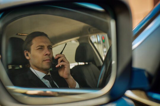 Close up of Caucasian businessman speaking on walkie talkie while sitting in car, coordinating transport or security operations. Ideal for corporate mobility or logistics campaigns