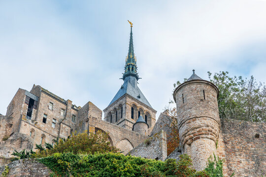Low angle view of Mont Saint-Michel Abbey with Gothic spire, medieval stone walls and fortified architecture in Normandy, France. Architectural history, cultural heritage, European travel