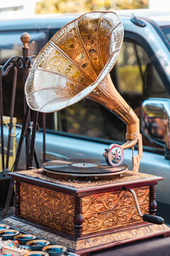 Vintage gramophone with an ornate brass horn and intricate wooden base on a market table. Horizontal