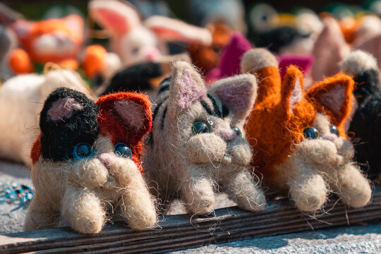 Handmade felted wool cats with colorful patches and blue eyes sitting on a wooden market stall. Horizontal