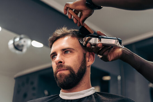 Close up of barber cutting fade hairstyle with electric trimmer in professional grooming salon