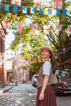 October 2024. Tbilisi, Georgia. Young woman standing on a cobblestone street under hanging Georgian and EU flags. Vertical