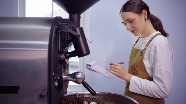 Female coffee roaster taking notes on clipboard near roasting machine