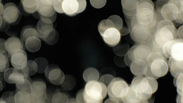 Abstract out of focus silver water bokeh background loop. Shimmering blurry light circles moving on dark backdrop for elegant overlay.