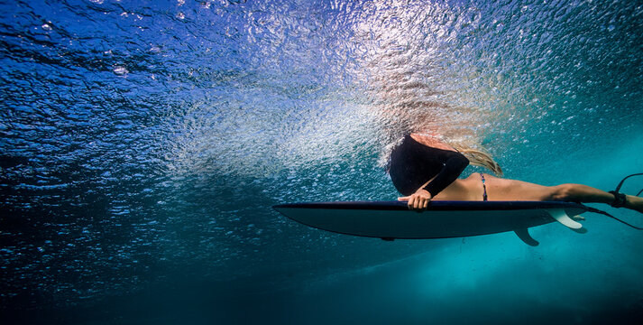Female Surfer Paddling Underwater With Surfboard In Deep Blue Ocean Sunlight