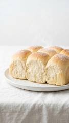 Fototapeta premium Freshly baked bread rolls steaming on ceramic plate over white linen in bright morning light