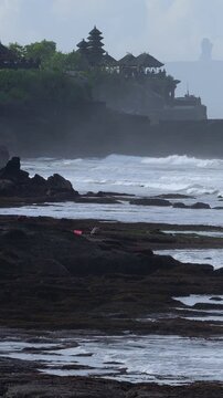 Swept Shoreline With Distant Tanah Lot Temple Silhouette, Rhythmic Waves And Foam Rolling Over Flat Rock Shelves, Long Lens Compression Creating Layered Cliffs, Bali, Indonesia, vertical video
