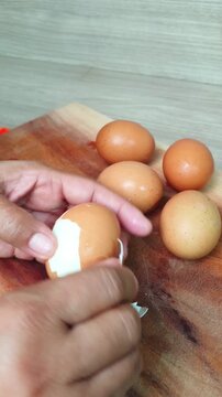 Peeling a hard-boiled egg on a wooden cutting board. Preparing fresh protein rich ingredients for breakfast cooking