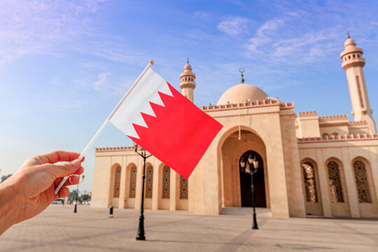 Hand holding Bahrain flag with Al Fateh Grand Mosque and palm trees in Manama
