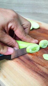 Slicing fresh green cucumber on a wooden cutting board with a knife. Prepping healthy ingredients for cooking and salad preparation