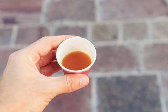 Hand holding a small disposable paper cup filled with an energizing espresso, symbolizing a quick break and refreshment