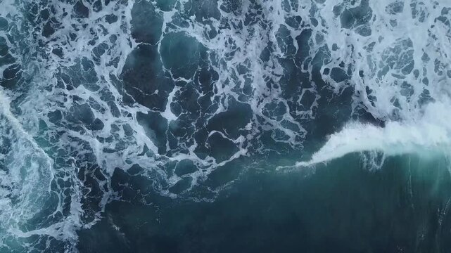 Aerial top down view of deep blue ocean waves crashing with white foam and swirling bubbles in motion.