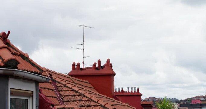Terracotta Rooftops Under Cloudy Sky: A close-up view of terracotta tiled rooftops with ornate chimneys under a dramatic, overcast sky, suggesting an urban or suburban landscape.