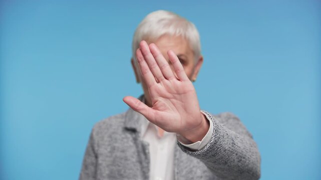 Senior Woman Making Stop Gesture Toward Camera on Blue