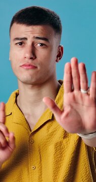 Face, man and hand gesture in studio for stop symbol, warning sign and rejection for negative opinion. Male person, palm emoji and caution for no entry, protection or disagreement on blue background.