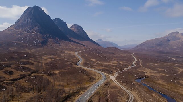 Aerial view reveals winding road through rugged mountains under a clear sky