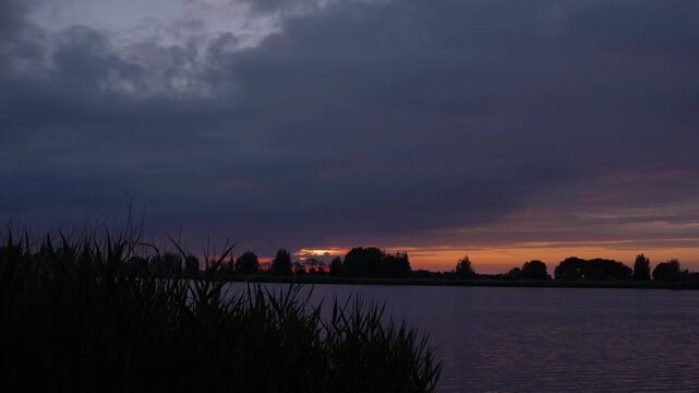Dramatic Sunset Over the De Lek River in the Netherlands, Dark Stormy Clouds with a Warm Golden Glow on the Horizon, Serene Riverside Landscape.