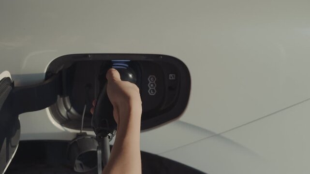 Close up of hand inserting charger plug into electric vehicle.