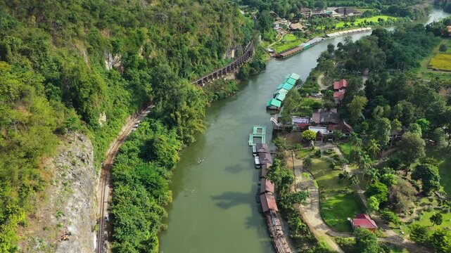 Aerial pullback of Krasae River with cliff railway and riverside resort in Thailand, drone reveals peaceful haunted landscape