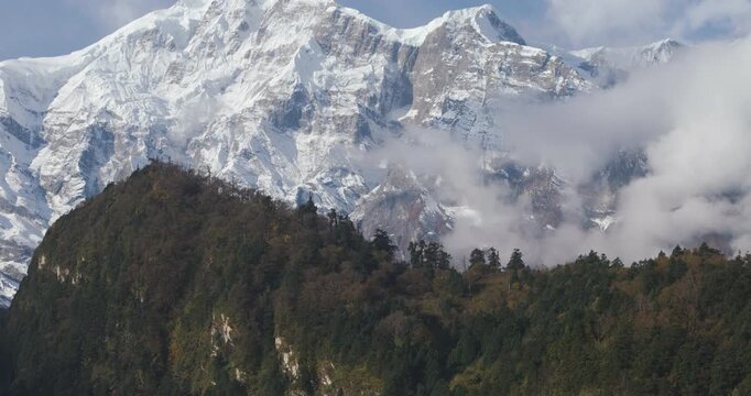 Annapurna Circuit Nepal, panoramic aerial view showing the massive snow covered rock face and alpine glaciers of Annapurna II peak towering above a forested ridge in the Manang region.