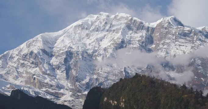 Annapurna Circuit, Nepal, aerial sideways tracking shot showing the massive snow-covered rock face and glaciers of Annapurna II peak against a blue sky near Manang.