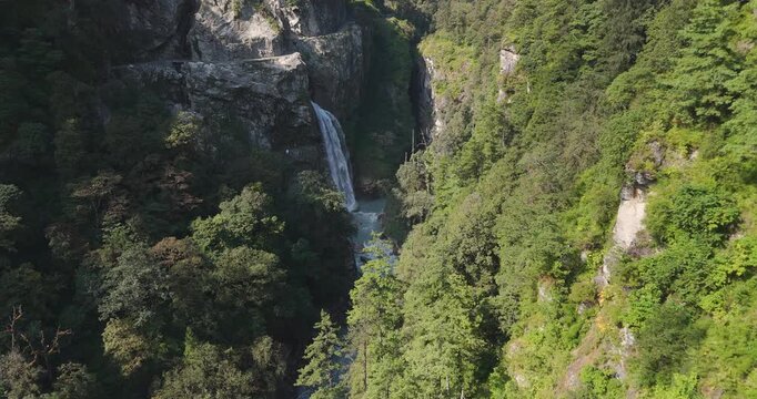 Annapurna Circuit Nepal, aerial push in shot of a jeep driving on the dirt road high above Danaque waterfall as it plunges down a rocky cliffside into the Marsyangdi River gorge in Manang.