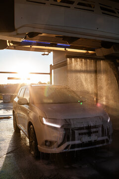 Vehicle covered in soapy suds and spray in automatic car wash bay in golden Australian light