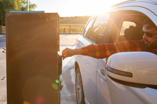 Man leaning from vehicle to tap debit card on car wash payment machine in golden light