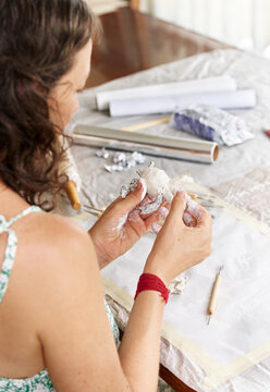 Focused young woman modeling small clay sculpture at table in her art studio. Creative hobby and handmade pottery concept.
