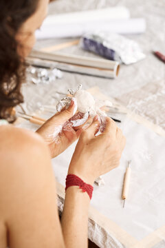 Focused young woman modeling small clay sculpture at table in her art studio. Creative hobby and handmade pottery concept.