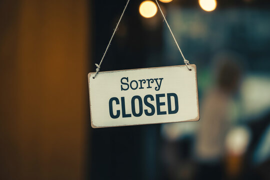 Vintage style closed sign hanging on glass door with blurry background lights for business closure.