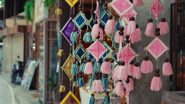 Colorful handmade hanging tassel ornaments decorating traditional village market, Decorative woven textile souvenirs with wooden beads swaying gently in outdoor craft shop 4k