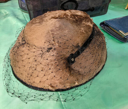 Elegant vintage women's brown fur pillbox hat with black birdcage veil on green satin background for retro fashion display.
