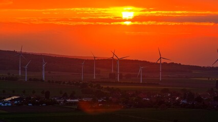 Wind Turbines at Dramatic Orange Sunset Over Rural Landscape