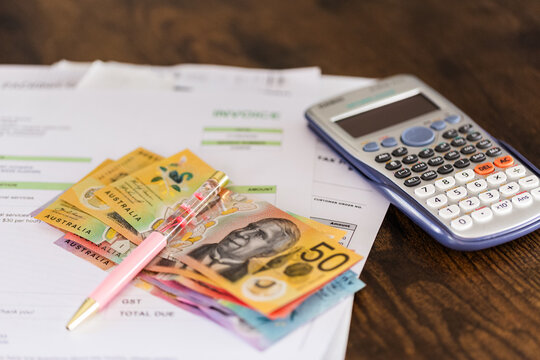 Small business invoices including GST sitting on deck with Australian cash and calculator