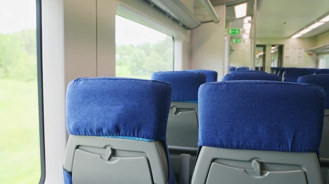 Blue upholstered seats inside modern train carriage with natural light and green landscape view