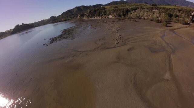 Aerial view of Koutu Boulders at low tide on the Northland coast of New Zealand, featuring sandy shoreline, coastal rock formations and calm sea in warm morning light.