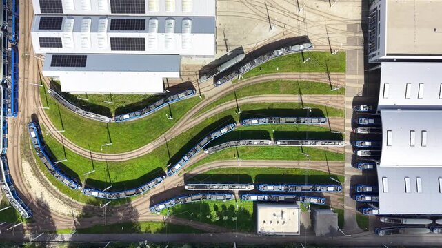 Aerial view of a tram depot showcasing multiple tram cars parked along curved tracks, with a large building featuring solar panels and green grass in the surrounding area