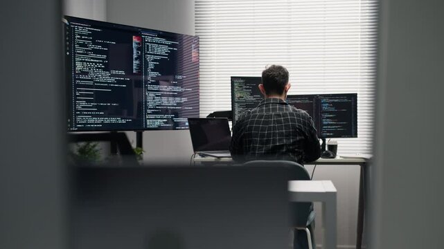 Behind view of Caucasian IT specialist engineer operating computer network infrastructure inside modern office interior.