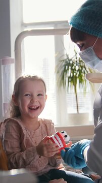 Girl, her mom and the dentist in the dental office, the stomatologist examining and consulting, daughter curious and docile