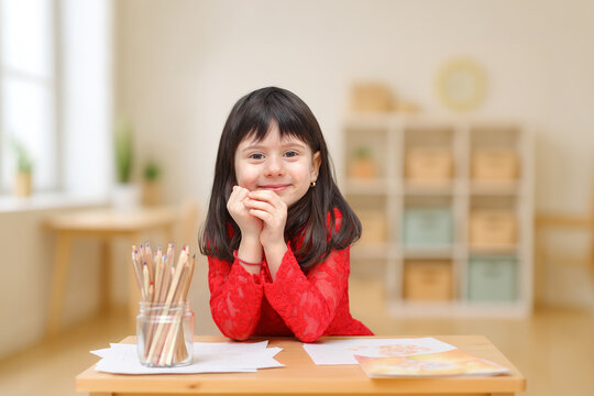 Smiling little girl drawing at classroom desk with colored pencils