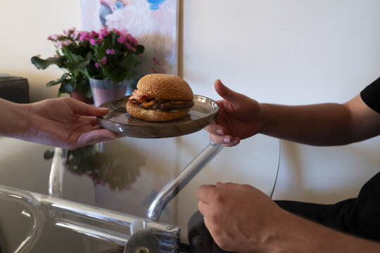 A delicious hamburger being served from one hand to another, accompanied by fresh flowers in the background, perfect for a food appreciation scene.
