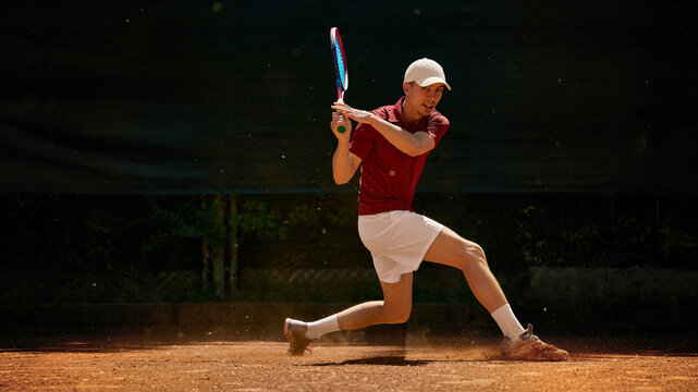 Tennis player sliding into backhand return on dusty clay court. Concept of clay court slide technique, defensive backhand play, footwear traction visuals and match pressure content.