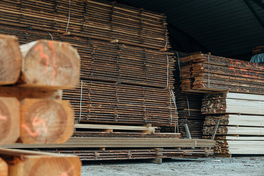 Close-up of stacked rough-sawn timber beams with marked end grain stored on spacers inside a sawmill warehouse. Visible wood texture and organized lumber inventory