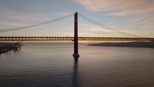 Silhouette of Ponte 25 de Abril red steel suspension bridge at sunrise over Tagus Estuary, Lisbon, Pied Avocets on Tagus Estuary Nature Reserve, Slow motion drone shot