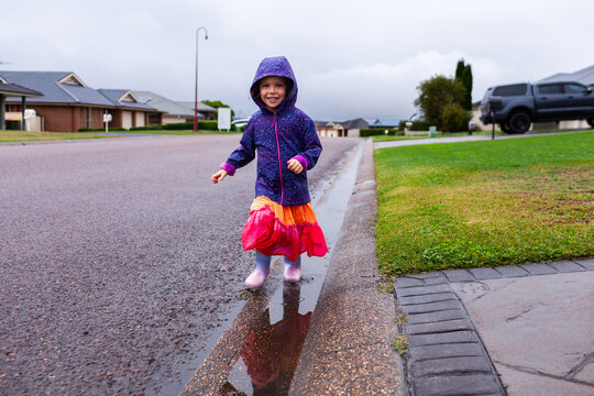 Happy child running and splashing through roadside gutter full of water on rainy autumn day