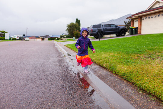 Happy child running and splashing through roadside gutter full of water on rainy autumn day